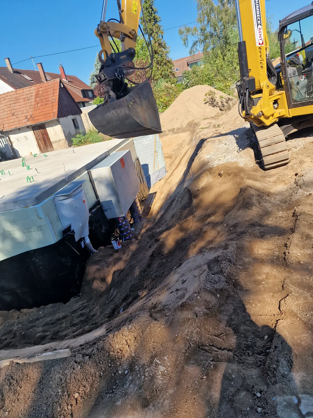 Minibagger hebt Erdreich für eine Baugrube neben einem Wohnhaus aus